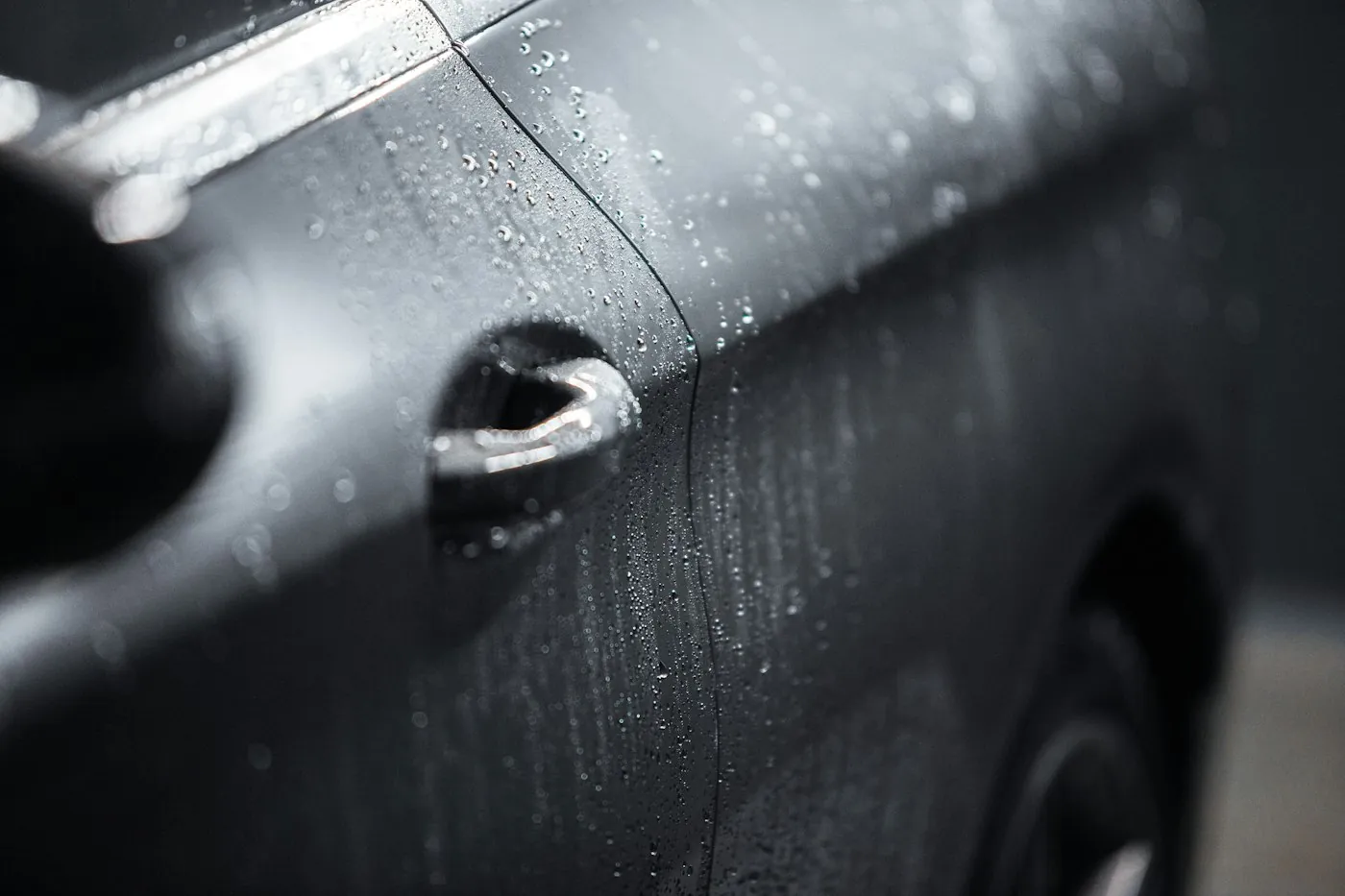 Water beading on the painted door of a dark car, close up