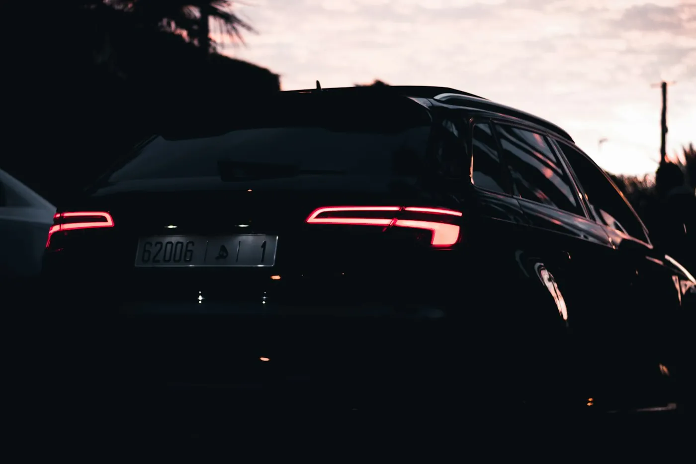 A dark coupe at dusk with red tail lights glowing