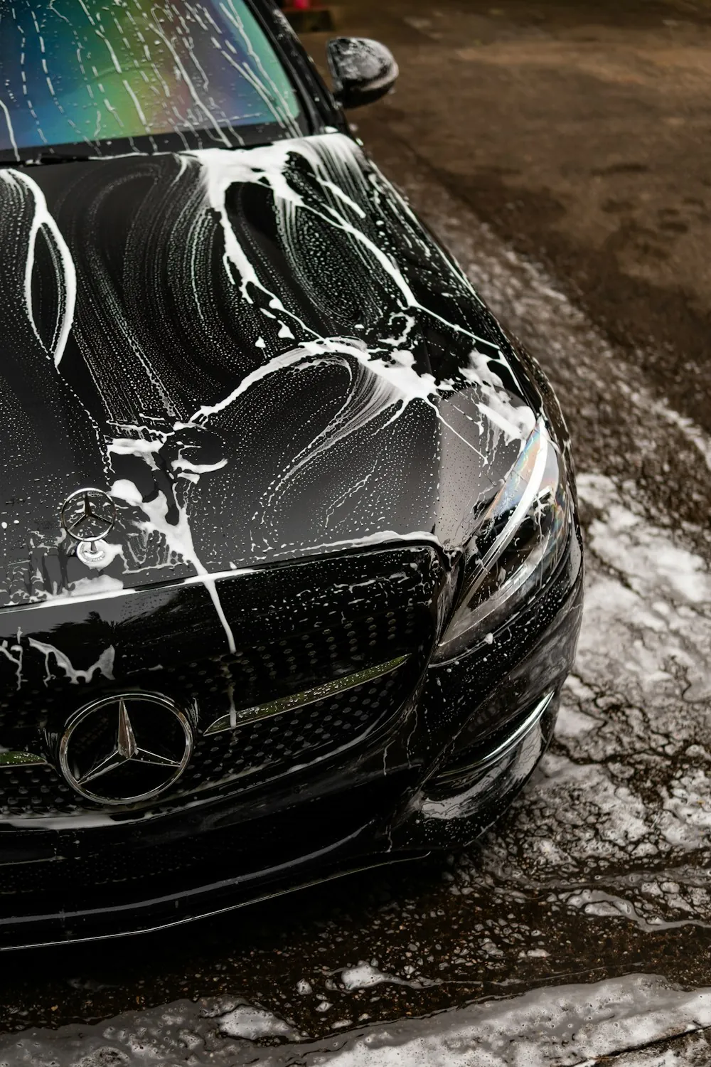 The front of a dark Mercedes covered in thick white foam during a hand wash