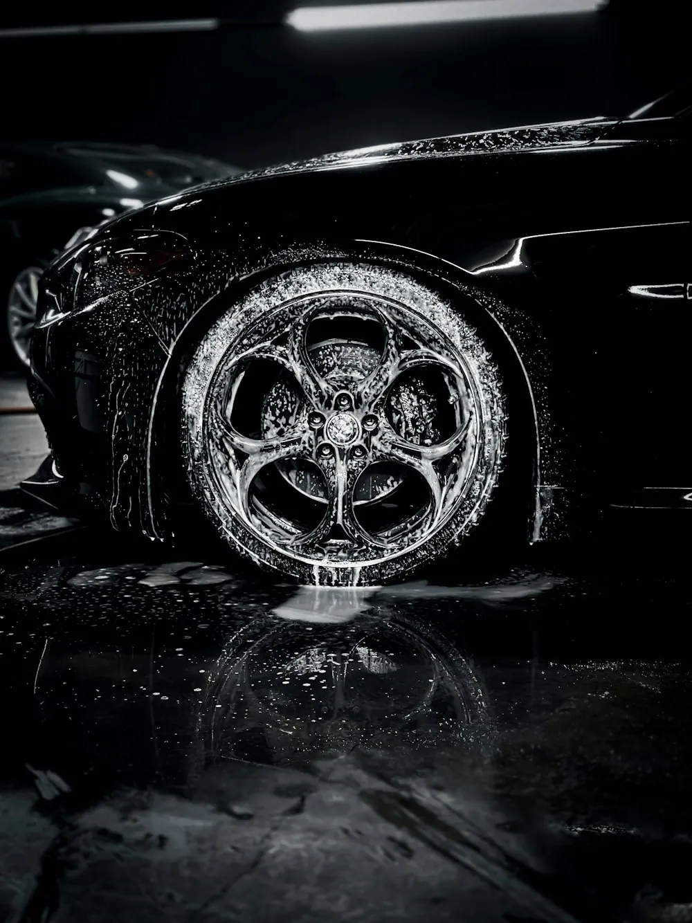 A wet alloy wheel covered in foam in the dark